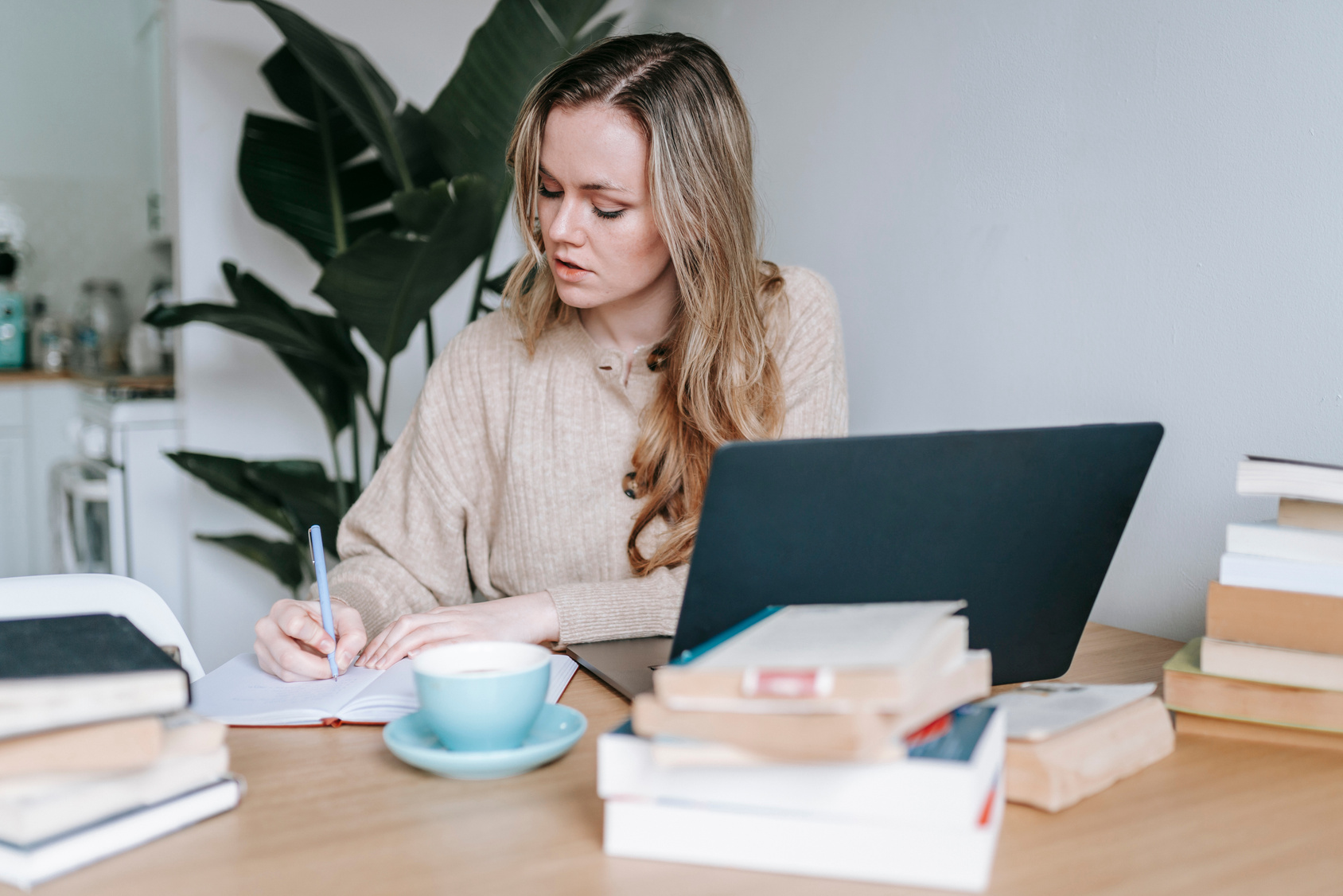 Pensive businesswoman writing information in notebook near laptop and coffee